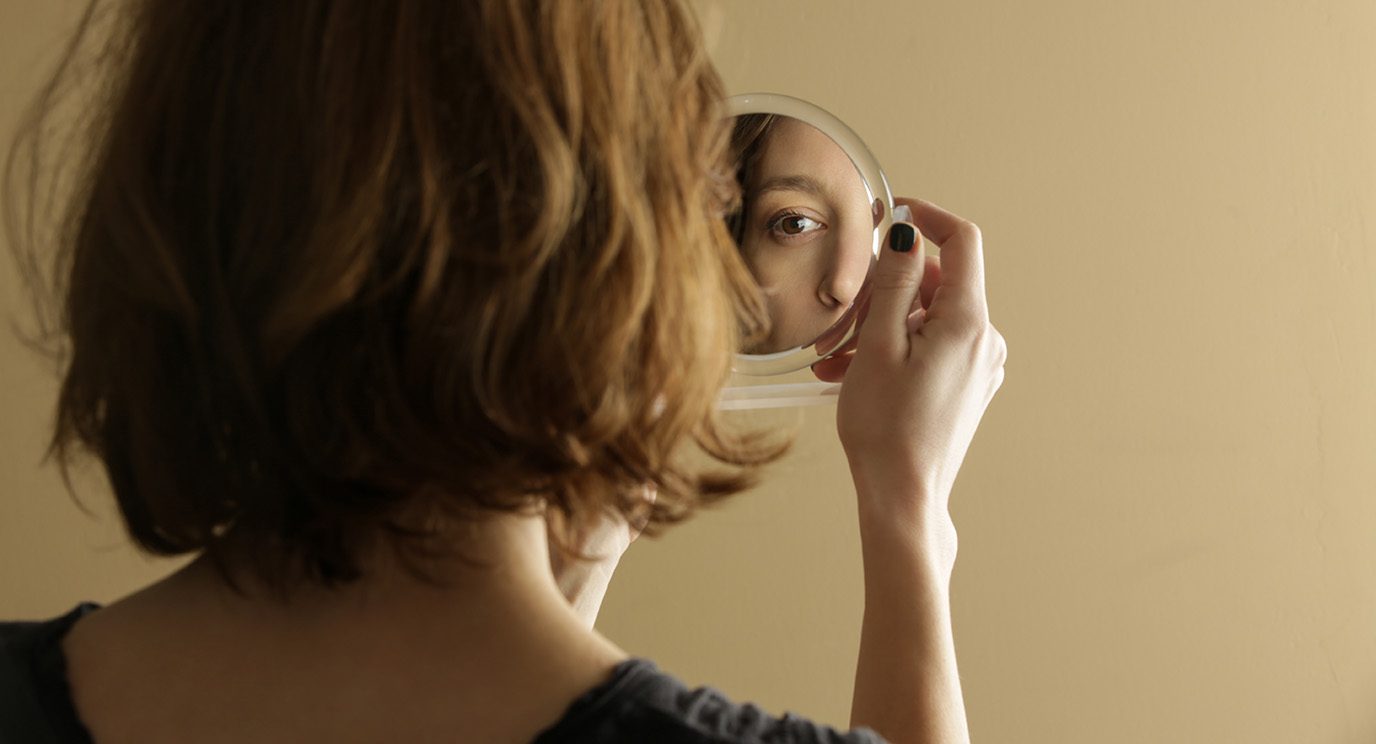 An unidentifiable woman looks at her reflection of herself in a hand mirror