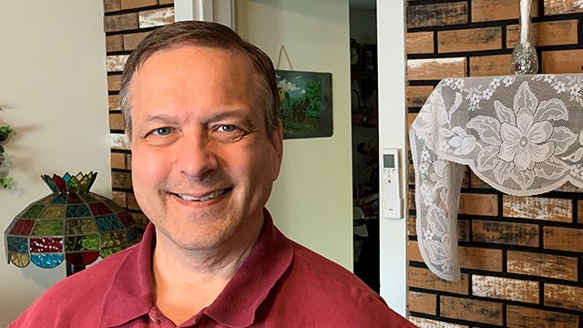 Throat cancer survivor George Brownfield, smiling in a home with a burgundy golf shirt on