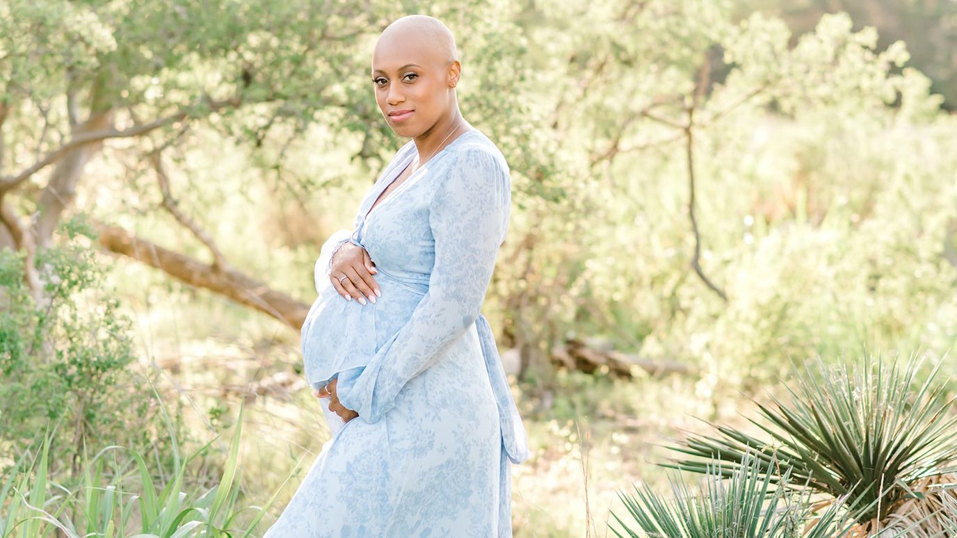 Breast cancer survivor Jasmine Grainger holds her stomach in front of outdoor greenery
