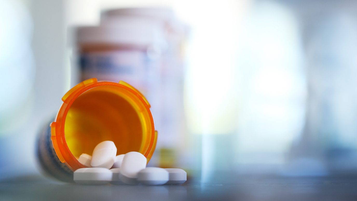 Blue-tinted photo of pill bottle on its side, spilling capsules, with additional blurry bottles in background