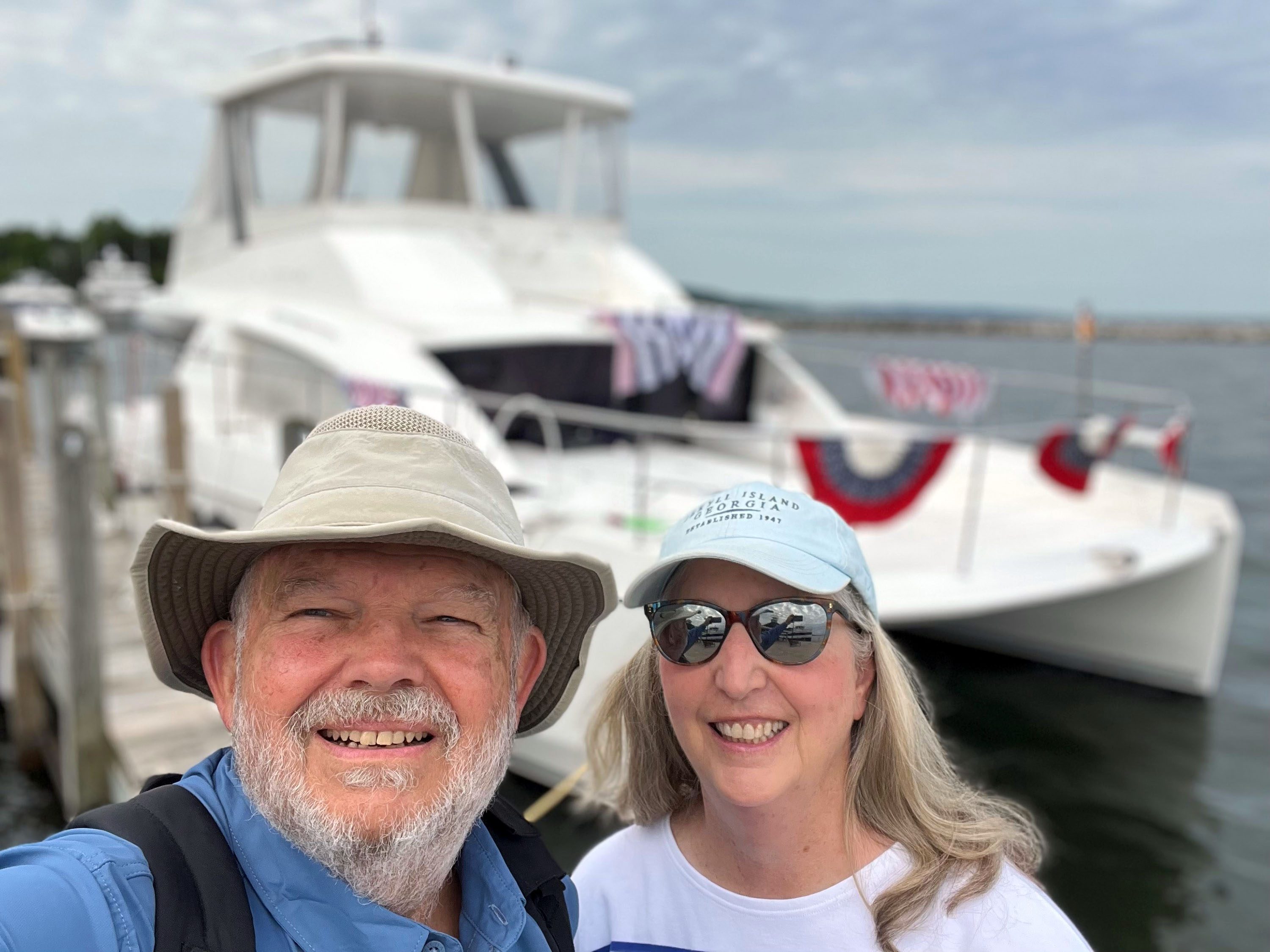 Paul McKinney and his wife, Mary standing in front of a boat on the water.