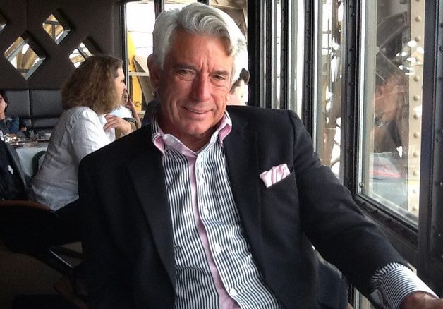 Buck Martinez sitting at a table at a restaurant wearing a black coat and white and striped shirt.