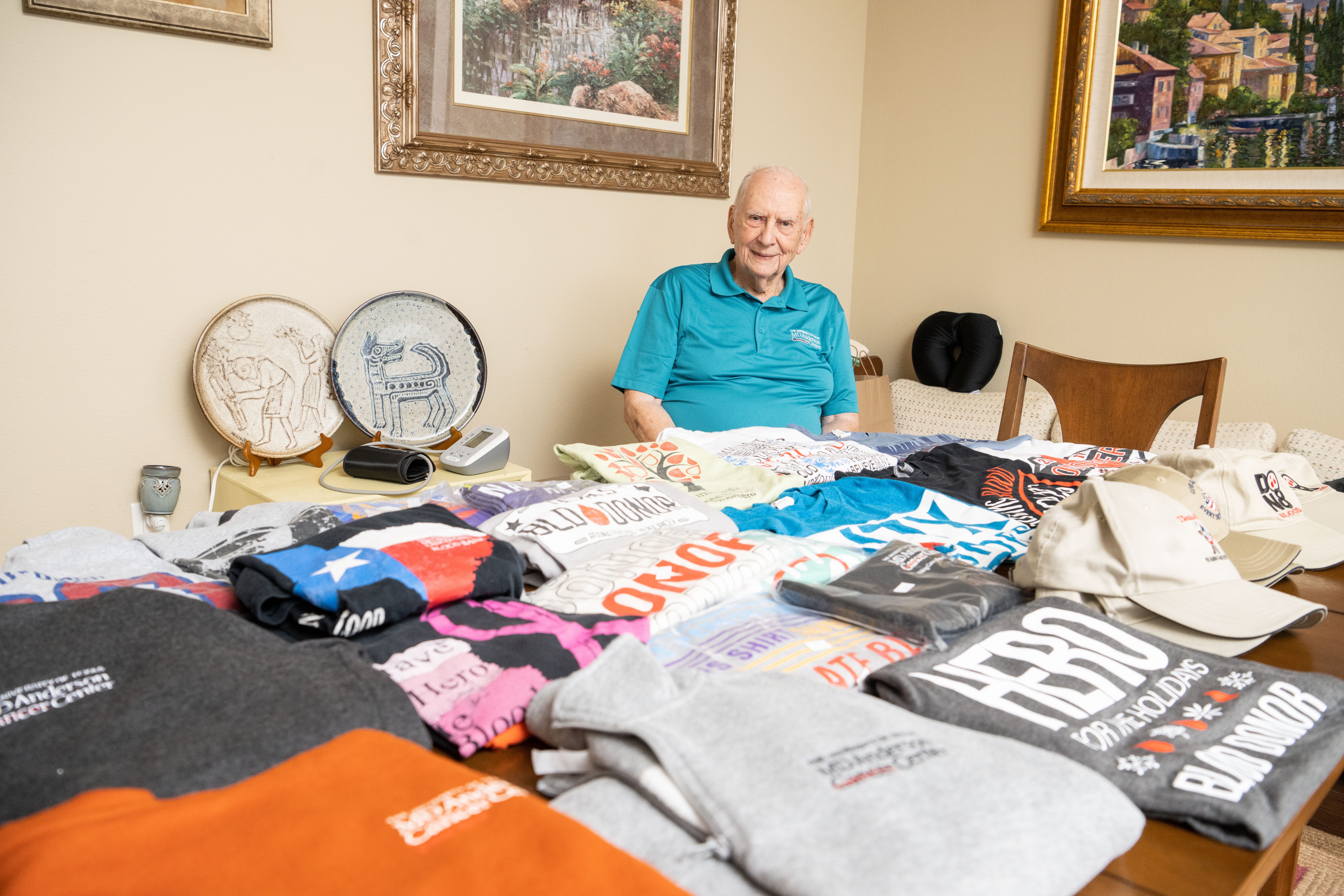 Tom Taylor sitting at a table Tom Taylor surrounded by MD Anderson blood donor t-shirts he's received over the years.
