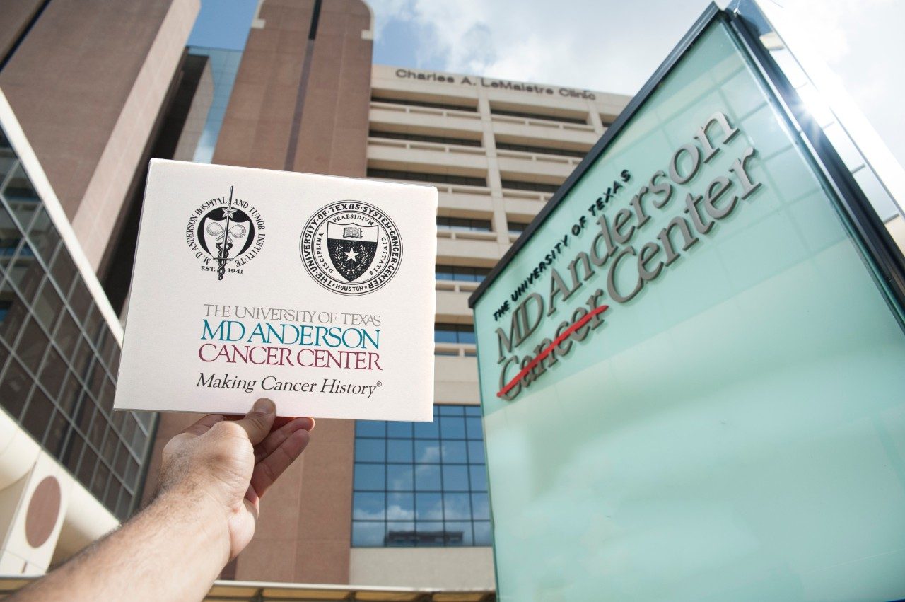 A card showing previous MD Anderson logos being held next to our current signage, which shows the current MD Anderson logo.