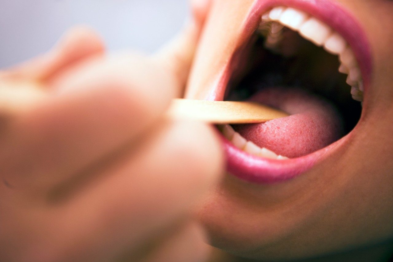 Close up of wooden tongue depressor in an open mouth