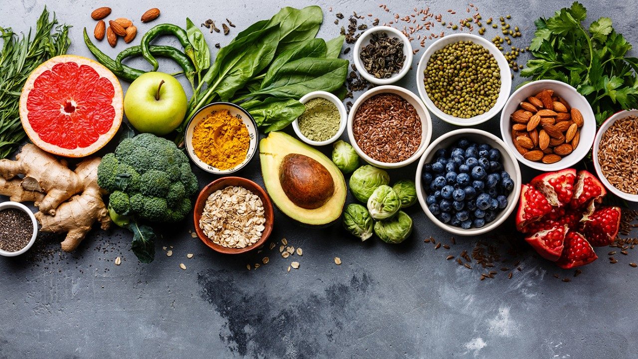 Healthy food clean eating selection: fruit, vegetable, seeds, superfood, cereals, leaf vegetable on gray concrete background.