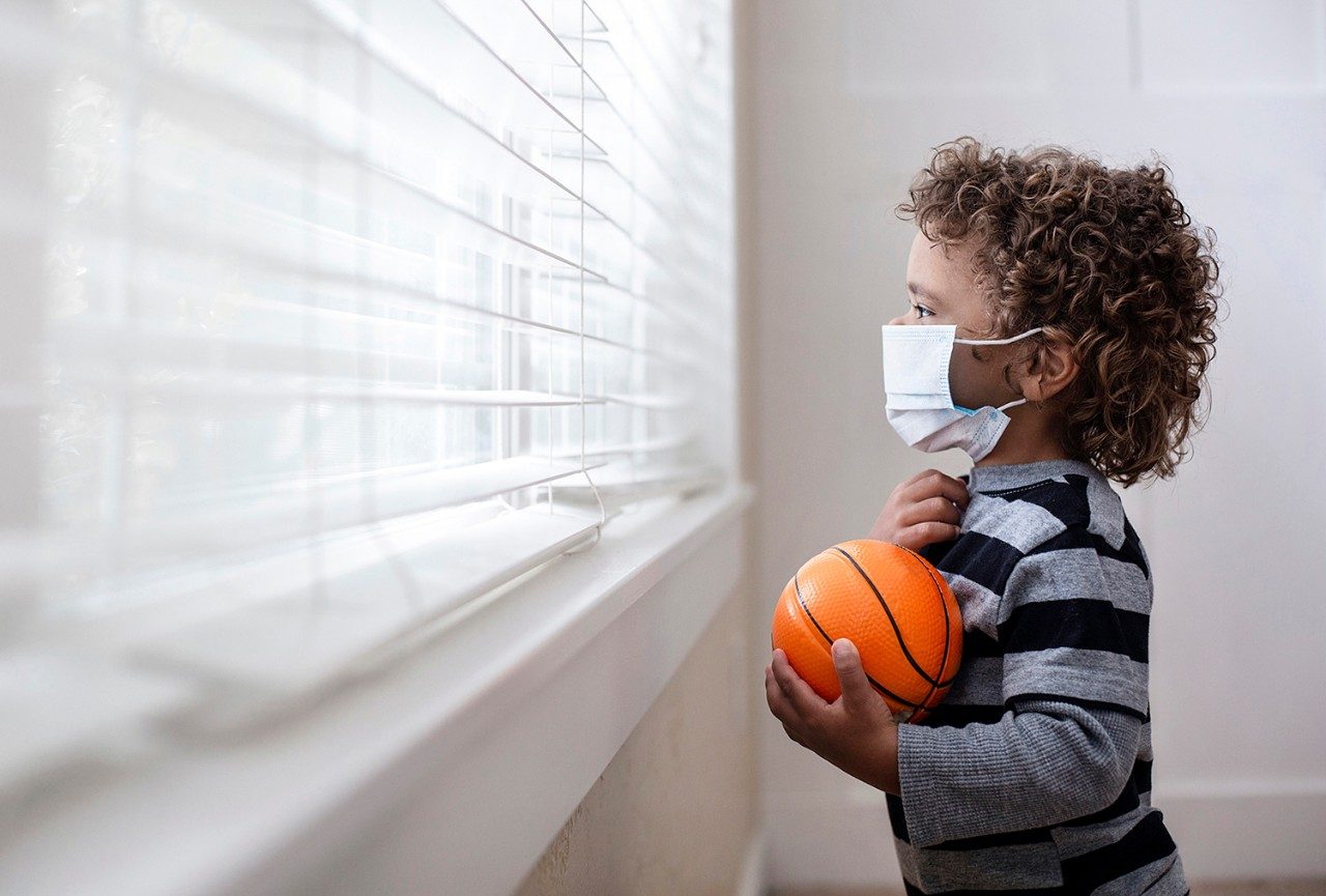 Toddler in mask holding basketball and looking out the window