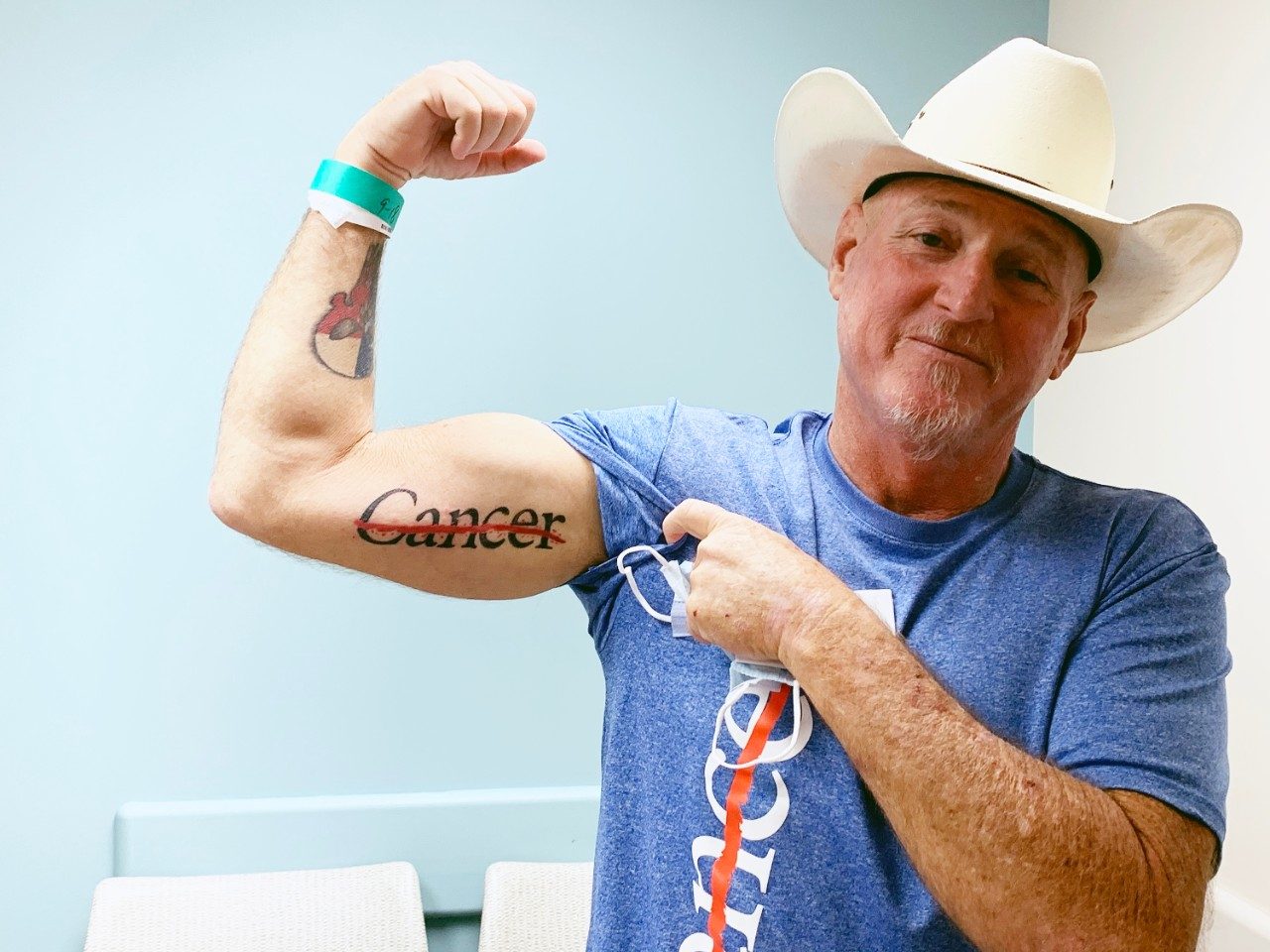 Tonsil cancer survivor Tim Hardesty flexes his arm to show his cancer strikethrough tattoo