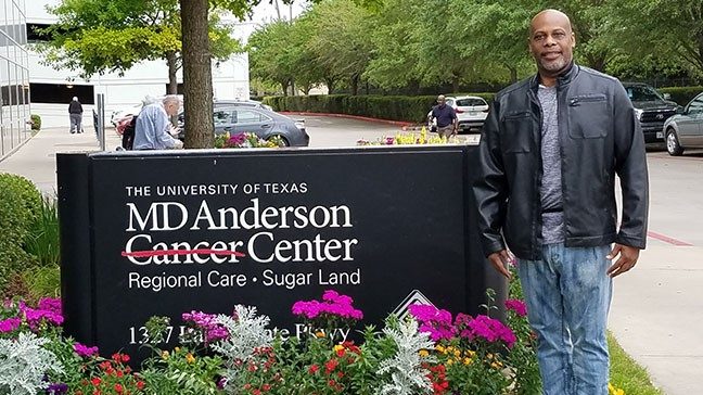 Pancreatic cancer survivor Drew Huggins standing beside MD Anderson in Sugar Land sign
