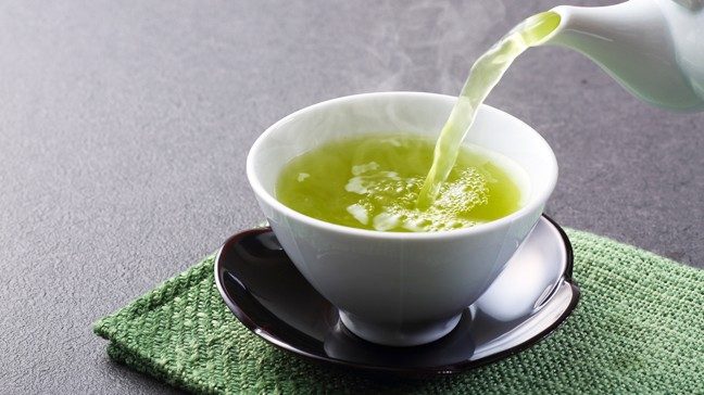 Green tea is shown being poured into a tea cup.