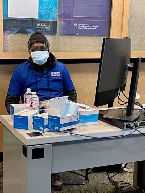 Man in blue jacket sits at computer in winter hat and face mask