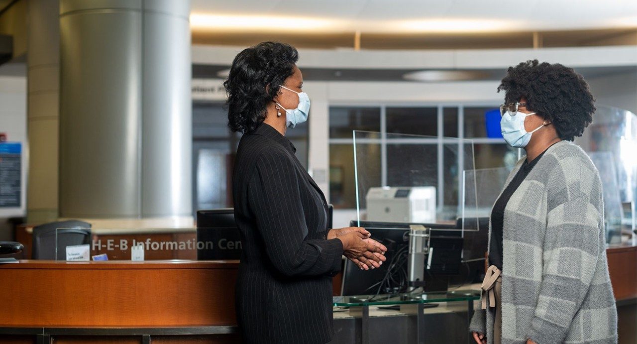 Debbie Wright (left) speaks with a colleague at MD Anderson while standing in front of the information desk.