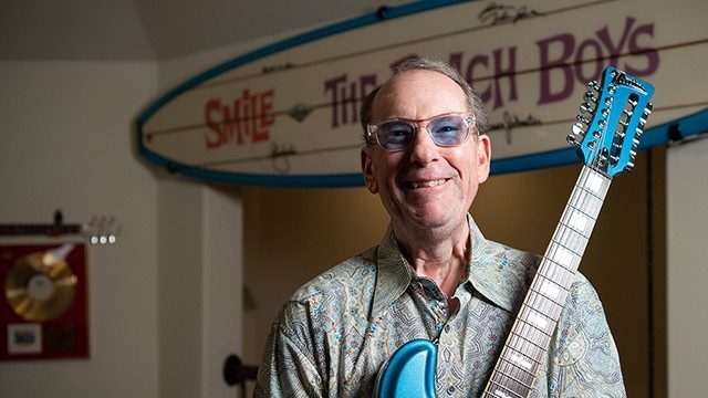 Anaplastic thyroid cancer survivor Jeffrey Foskett smiles at the camera while holding his guitar