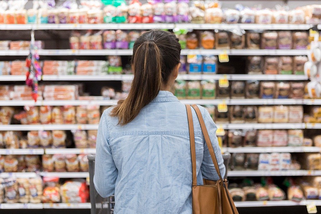 Woman is shown from behind looking at shelves in a grocery store.