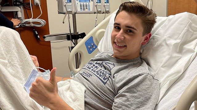 20-year-old colorectal cancer survivor Jaystan Davis, smiling and giving the "thumbs-up" sign from his hospital bed