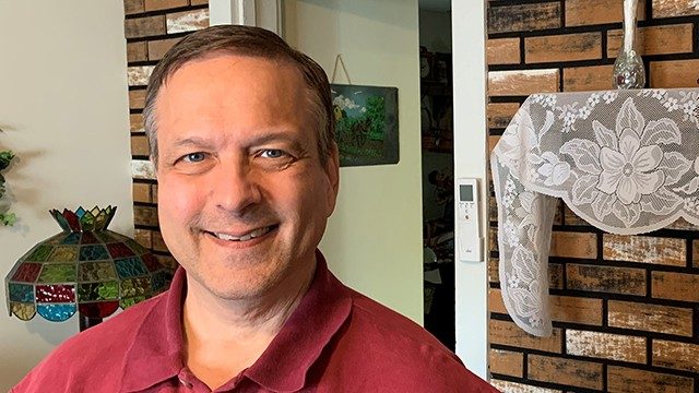 Throat cancer survivor George Brownfield, smiling in a home with a burgundy golf shirt on
