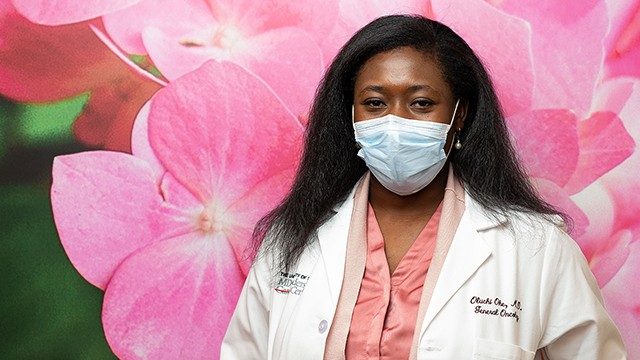 Breast medical oncologist Oluchi Oke, M.D., against a background photo of oversized pink flowers