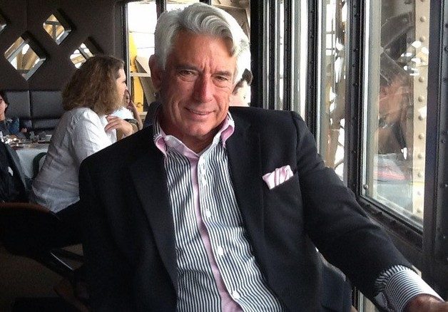 Buck Martinez sitting at a table at a restaurant wearing a black coat and white and striped shirt.