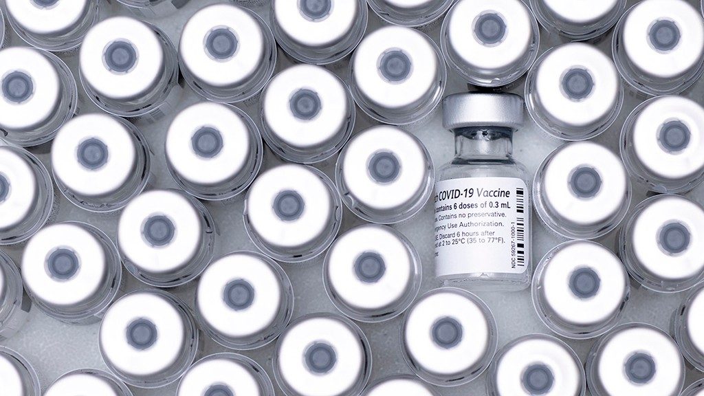 Bird's-eye view of the round silver top of dozens of vaccine vials, with one laid on its side for contrast