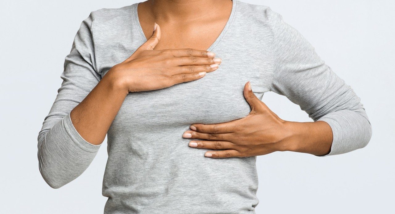 Torso shot of young person in gray 3/4 sleeve T-shirt palpating her left breast with both hands