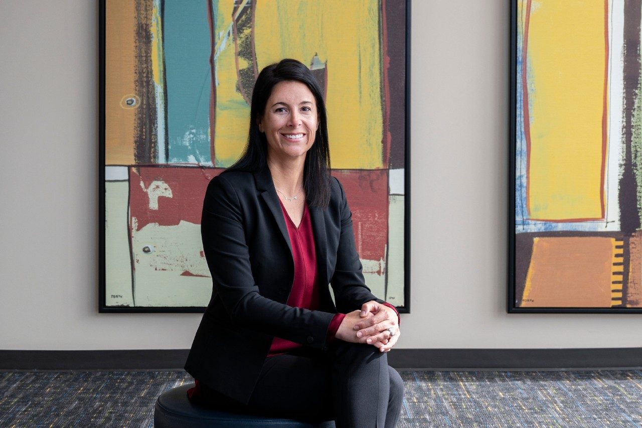 Courtney Holladay sits in front of a painting with her hands folded on her knee.
