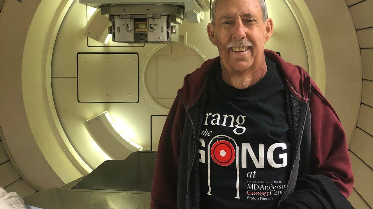 Stage IV salivary gland cancer survivor Glen Haubold stands in front of the proton therapy machine at MD Anderson in 2019.