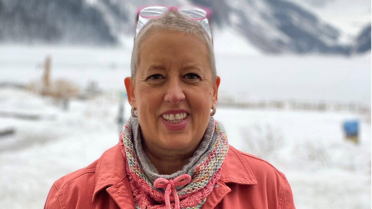 Triple-negative breast cancer survivor Joan Corson smiles in front of snow-covered mountains