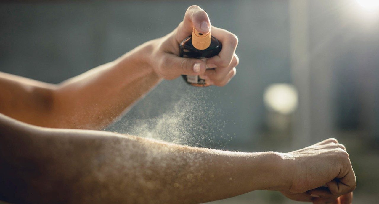 Close-up view of a person's two bare arms, one spraying the other with mist from a bottle