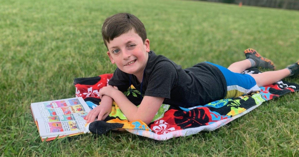 Benjamin Lowe lying on a towel and reading a book outside.