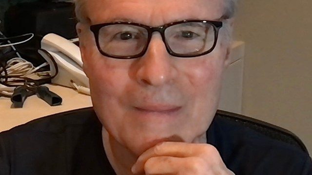 Six-time cancer survivor Arthur Hamberger, M.D. poses in a black T-shirt and black-framed glasses