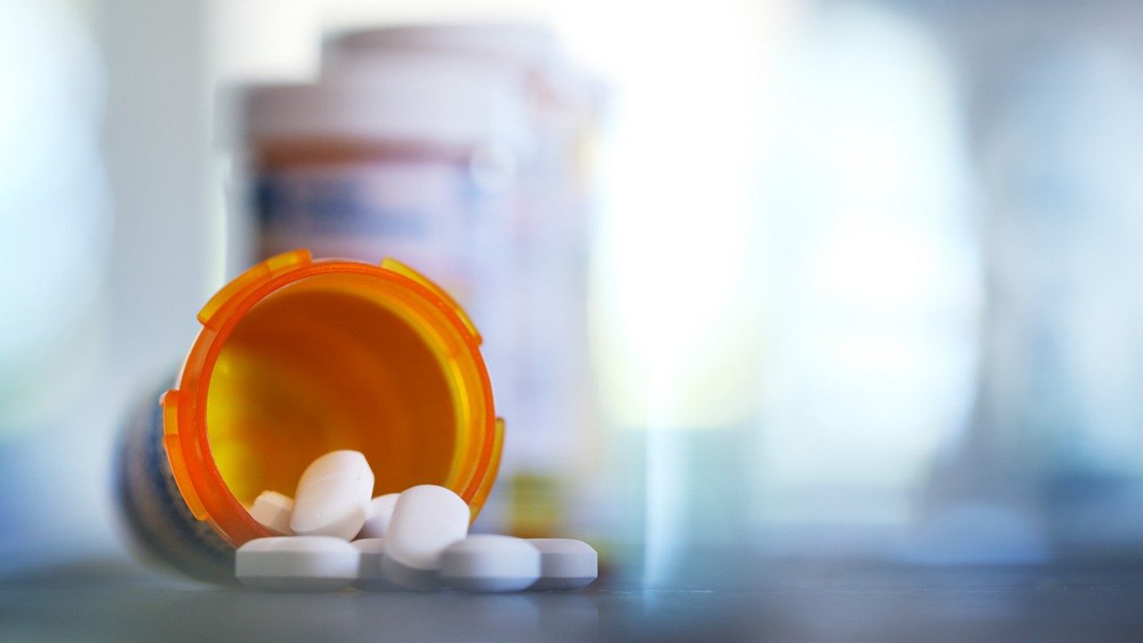 Blue-tinted photo of pill bottle on its side, spilling capsules, with additional blurry bottles in background