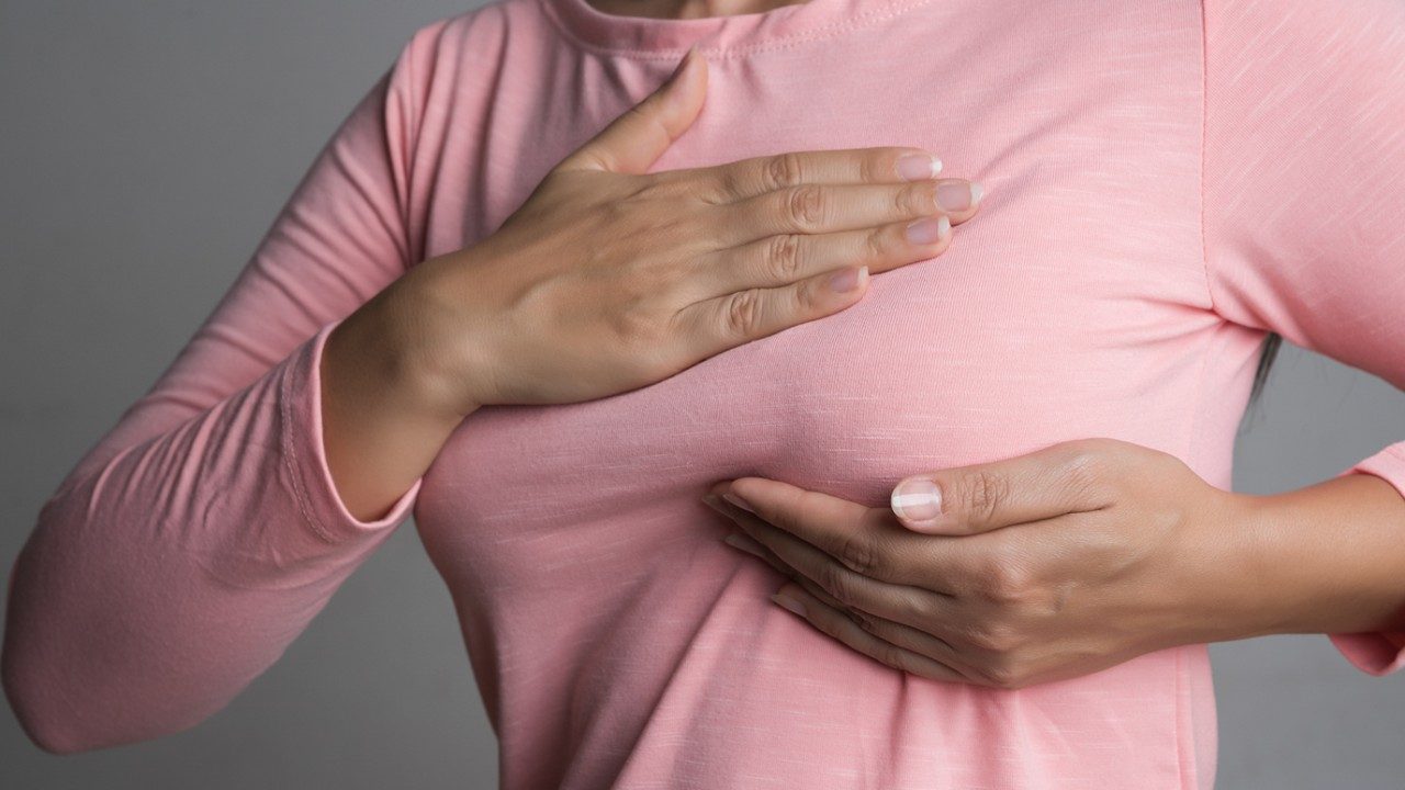 Woman in pink long-sleeved shirt palpates her left breast