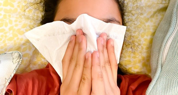 Person using both hands to cover their face with a tissue