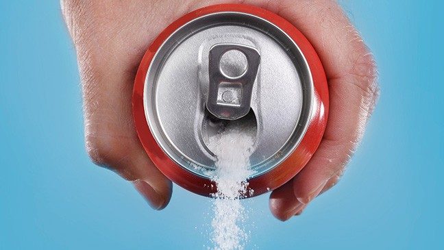 A hand holds a red can of soda against a bright blue background. Instead of soda, granulated sugar is being poured out of the soda can.