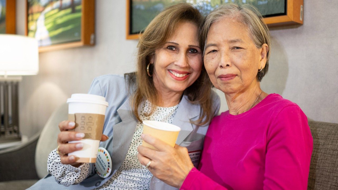 Two women sitting together each holding a cup of coffee