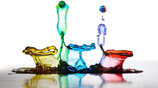 Drops of yellow, green, blue, purple and red food dye being added to water.