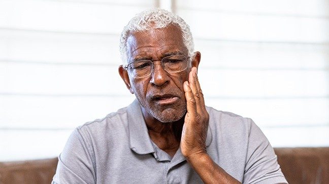 Older black man rubbing the side of his jaw in pain