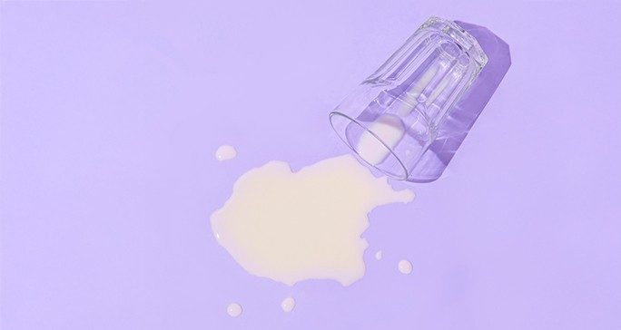 A glass of spilled milk against a purple background.
