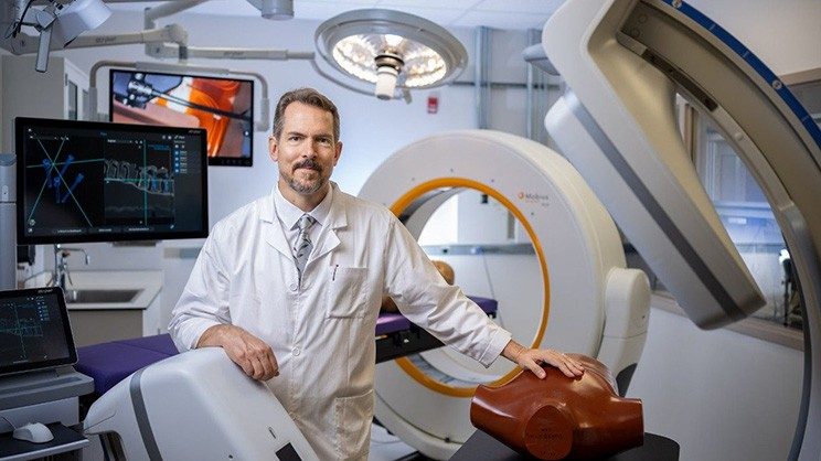 A man in a white coat stands in an operating room