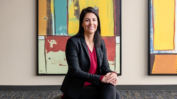 Courtney Holladay seated with legs crossed and hands clasped over her knee.
