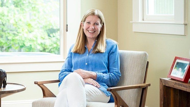 Dr. Schmeler smiles while sits in a chair with her legs crossed.