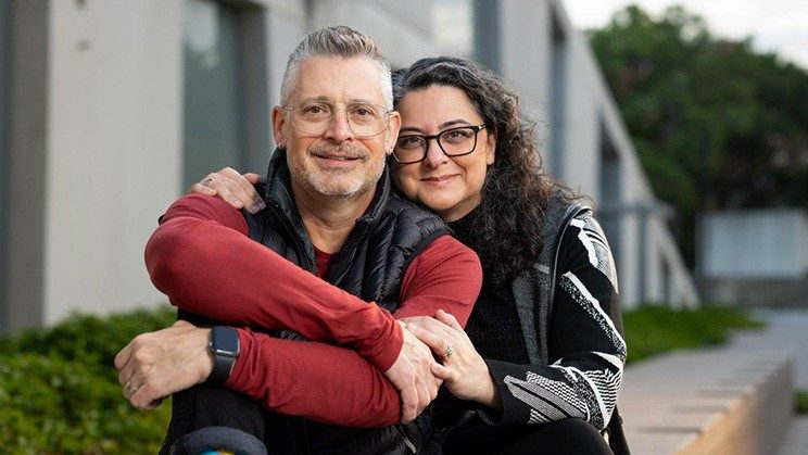 A woman in a black and white sweater with her arm around a man in a red long sleeve shirt and black vest