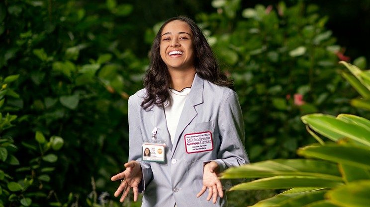 Saloni Cholia smiling, wearing an MD Anderson volunteer jacket and standing in a garden