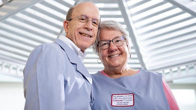 A smiling man and woman wearing blue MD Anderson volunteer apparel