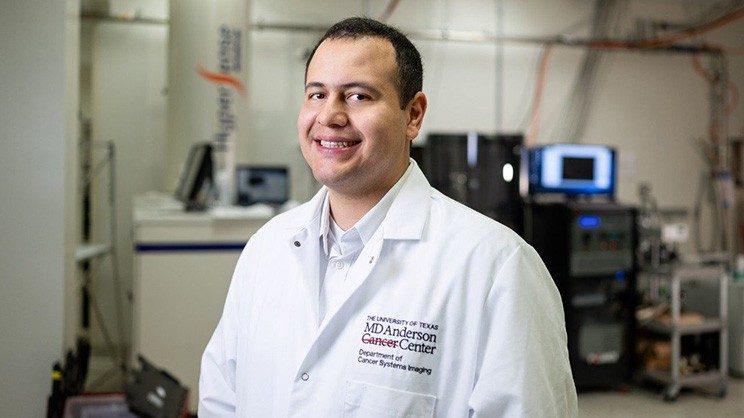 Smiling man in a white coat stands in a room with research equipment