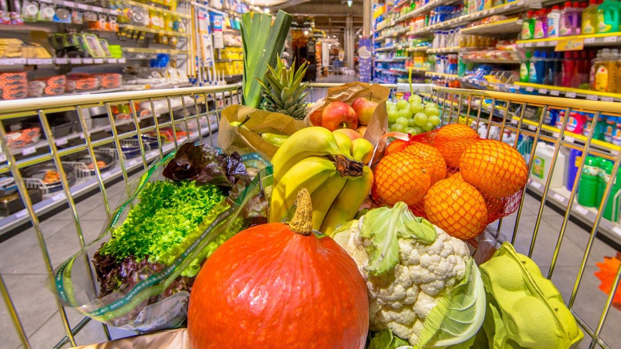 Grocery cart with fresh fruit and vegetables in it, in grocery store