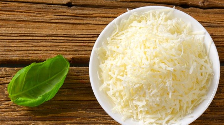A bowl of fresh grated parmesan cheese on a board with a basil leaf.