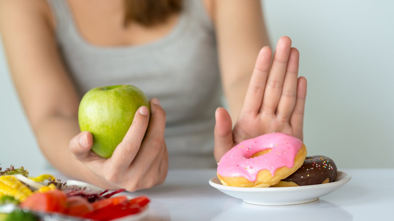 Woman holds apple in one hand and refuses donuts with the other