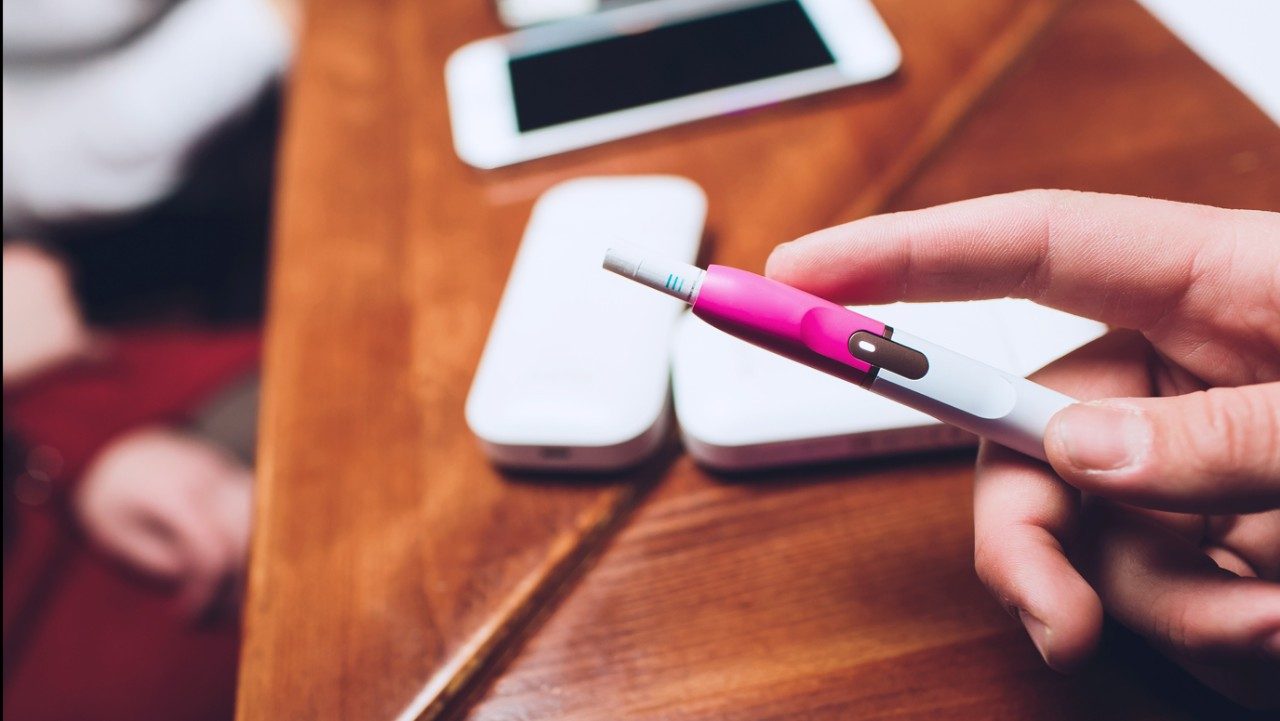 Woman's hand holding a pink IQOS device