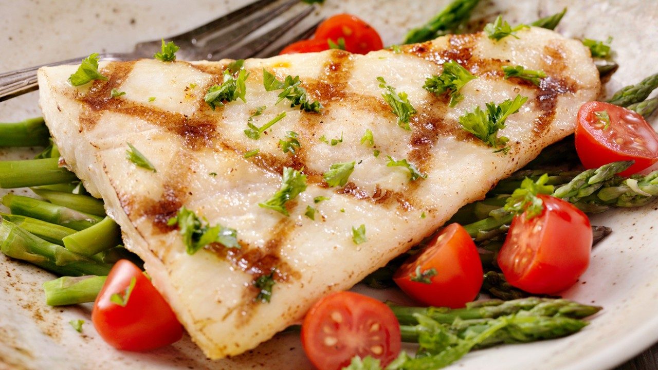 Grilled filet of white fish on plate with tomatoes and asparagus.